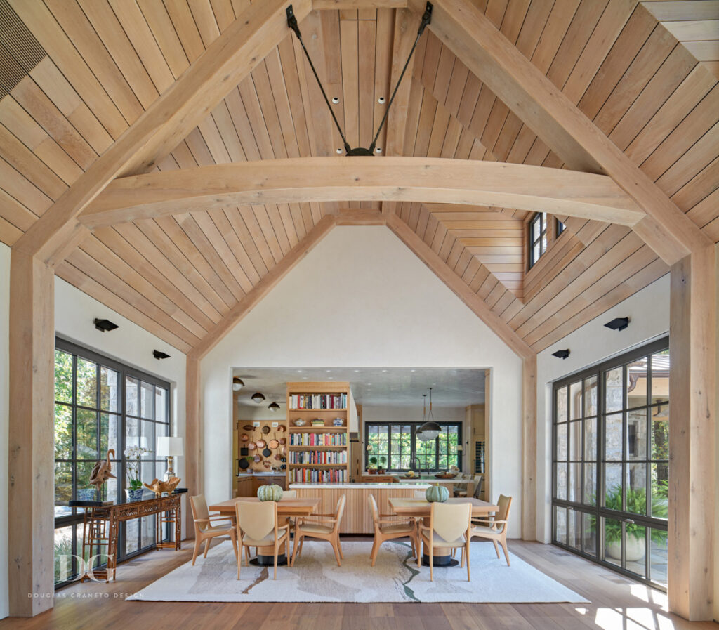 Wood paneled vaulted open plan dining area with custom kitchen in the background. Dining table and cabinetry by Rock Ridge Fine Cabinetry and chairs by Artistic Frame