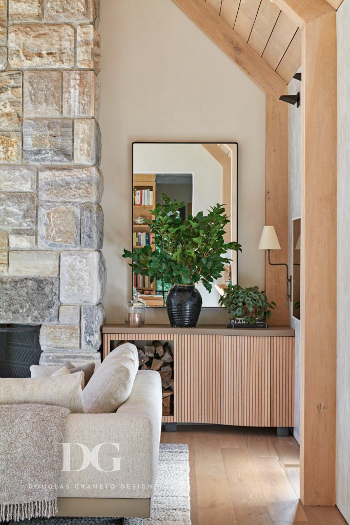 View of corner of Minotti DDC sectional with a Rosemary Hallgarten throw, a stone clad fireplace and custom built-in log storage